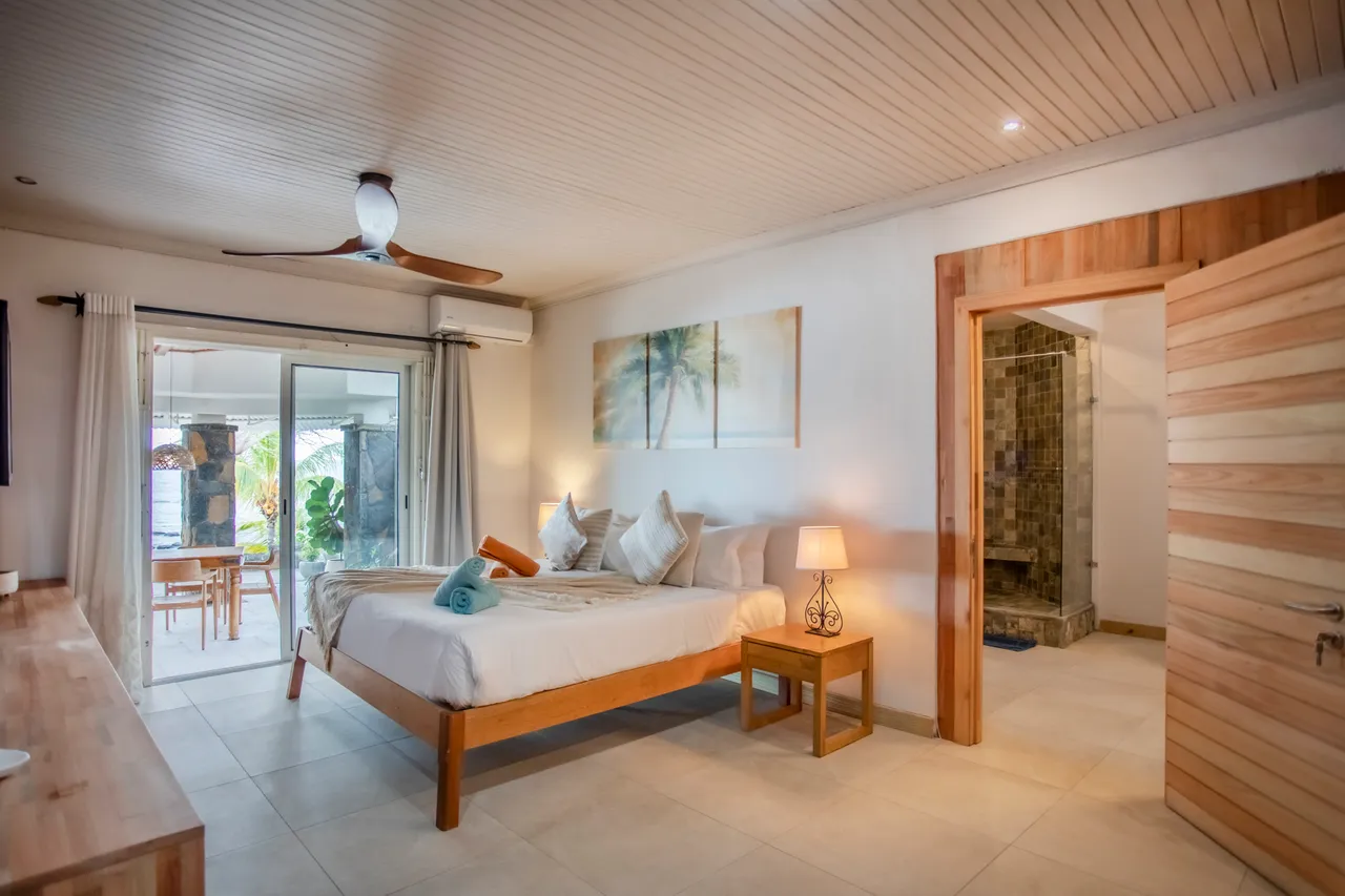 Chambre composée d'un lit double et d'un mobilier en bois clair. Accès direct à une terrasse vue jardin. Salle de bain attenante avec douche en mosaïque.