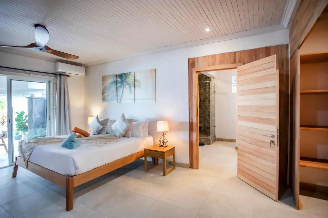 Chambre avec lit en bois et draps clairs. Accès à un patio extérieur.