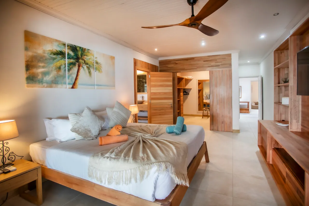 Chambre avec lit en bois, draps clairs et éclairage doux. Accès à une salle de bain attenante.