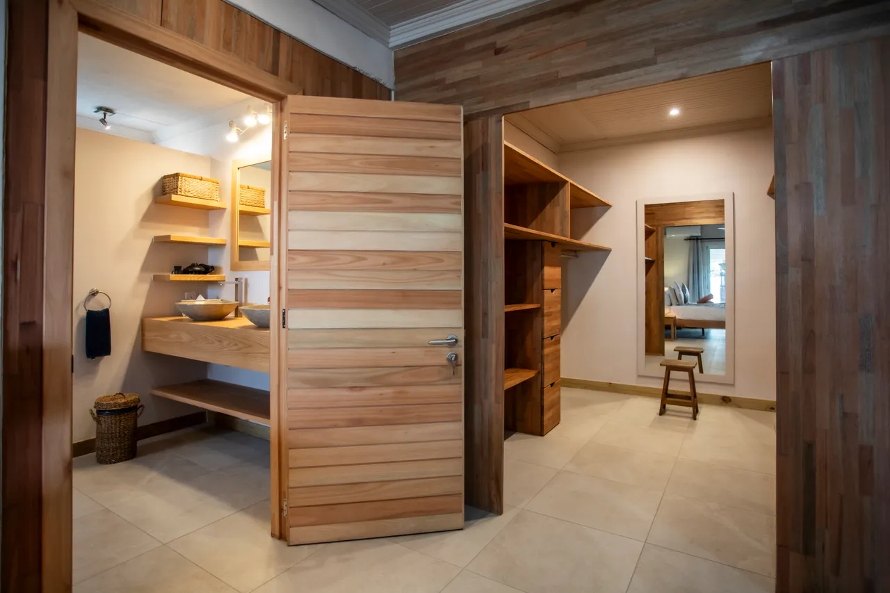 Salle de bain fonctionnelle avec lavabo en bois et miroir. Rangement intégré pour un espace organisé. Accès à une chambre adjacente.