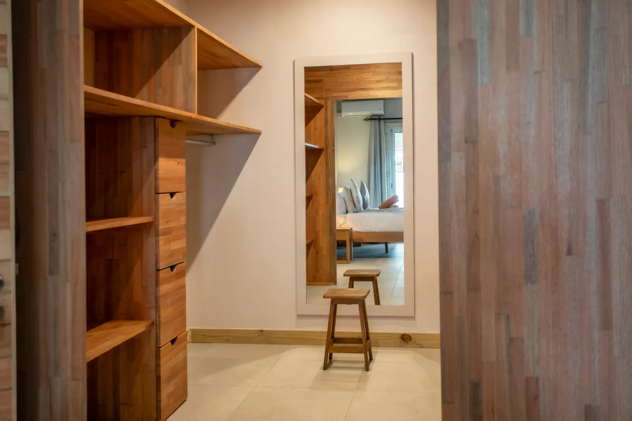 Espace de rangement intégré avec étagères en bois et miroir. Accès direct à la chambre.