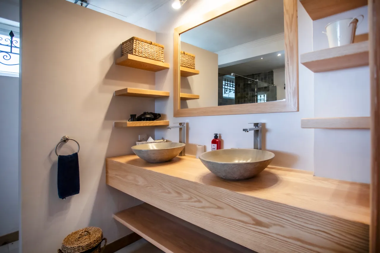 Salle de bain avec double vasque en métal et étagères en bois. Miroir large et espace de rangement pratique. Éclairage doux pour une ambiance apaisante.