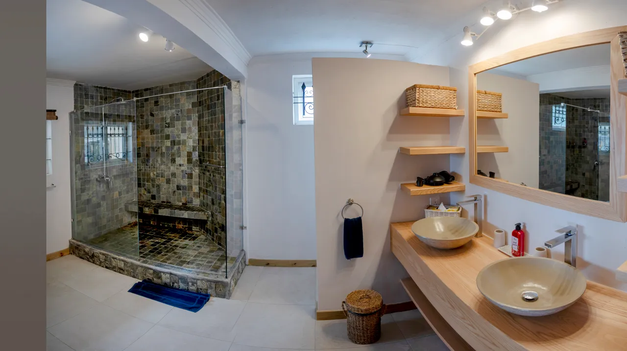 L'espace de la salle de bain comprend une douche carrelée et un double lavabo. Étagères en bois pour un rangement organisé. Miroir large offrant une bonne luminosité.