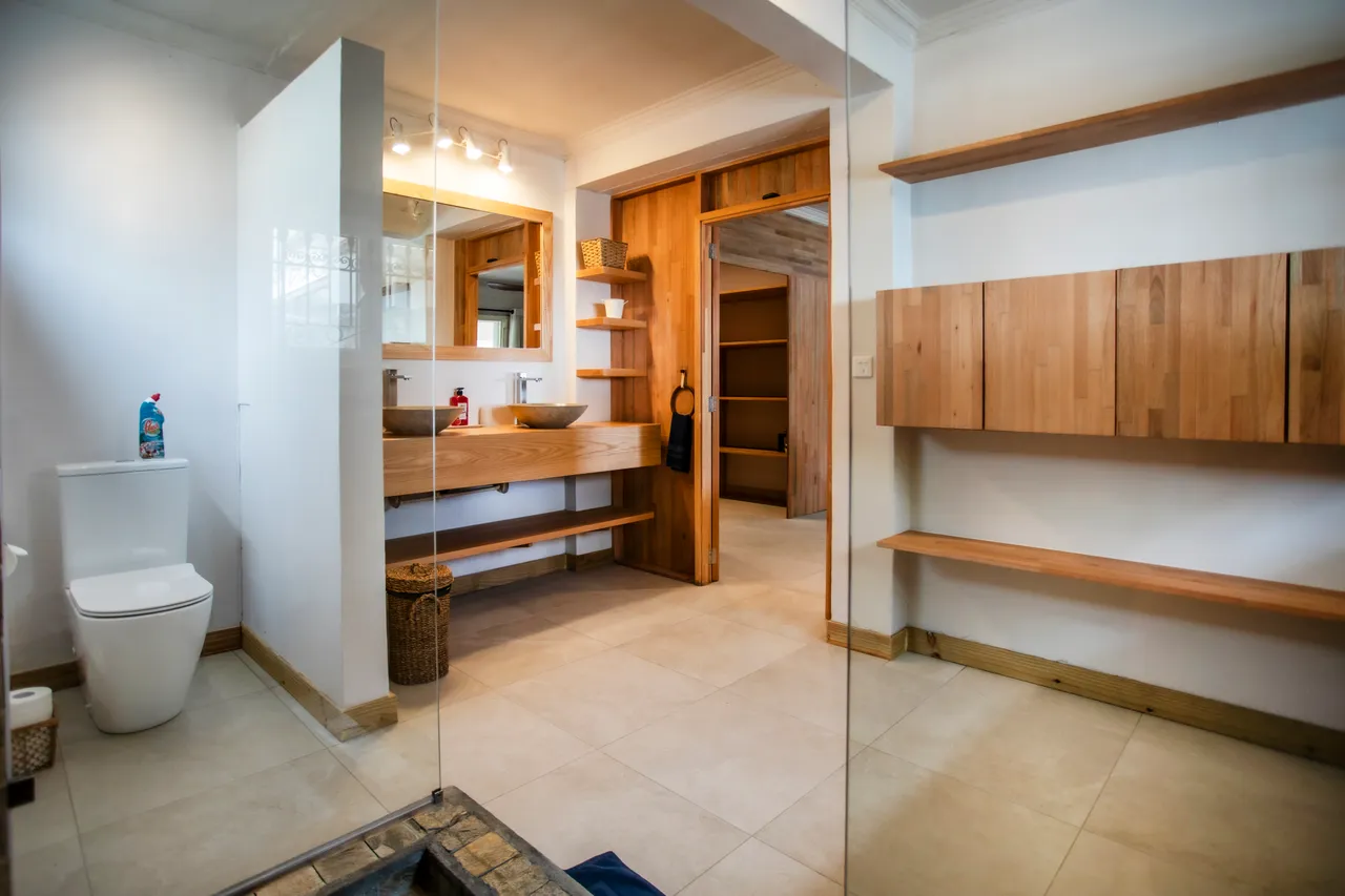 Salle de bain moderne avec double vasque et miroir lumineux. Étagères en bois pour un rangement optimisé. Douche carrelée avec accès facile.