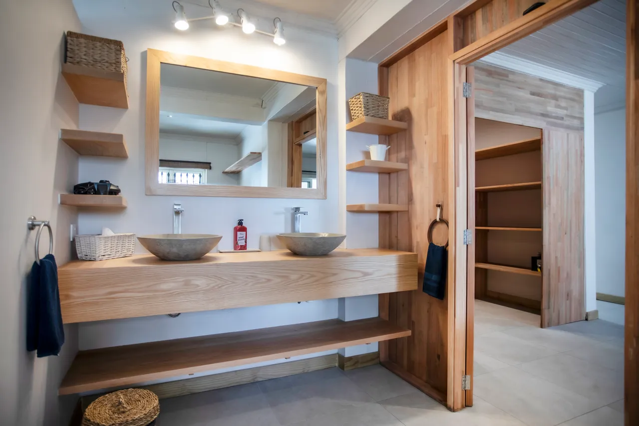 Salle de bain équipée de deux vasques en pierre et miroir éclairant. Rangement pratique avec étagères en bois. Douche carrelée avec séparation en verre.