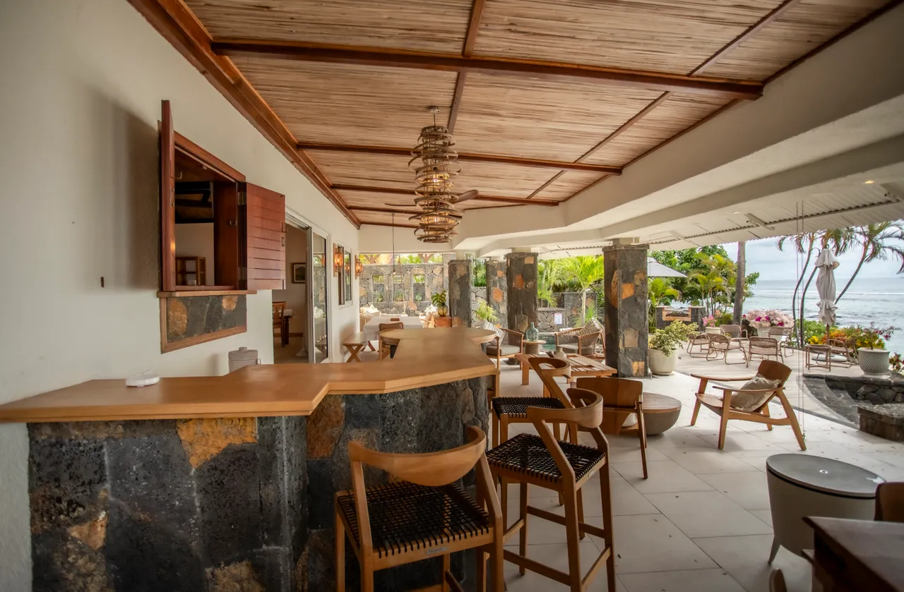 Espace de vie ouvert avec un bar en bois et vue directe sur la mer. Mobilier confortable et éclairage naturel créent une atmosphère agréable.