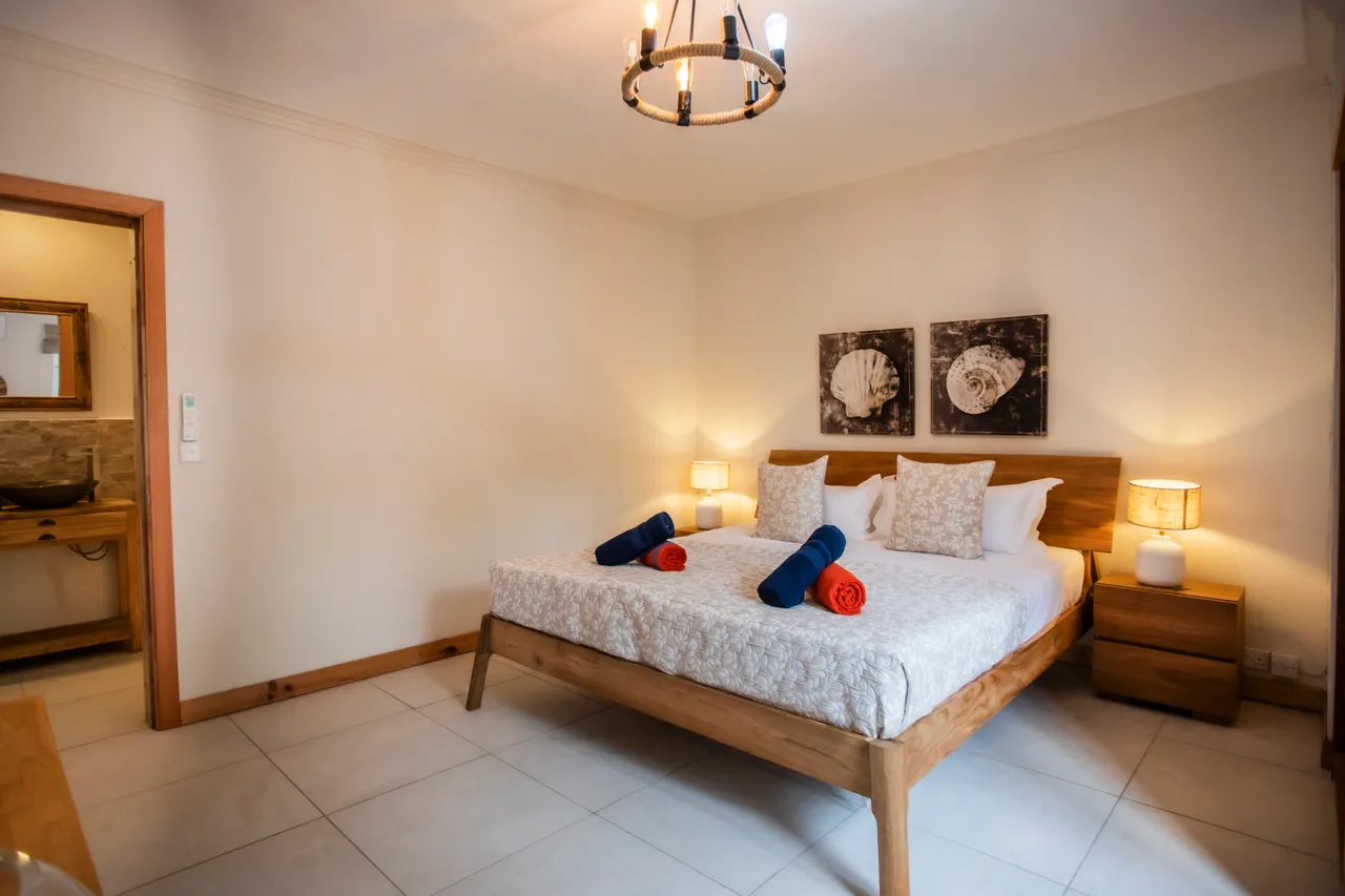 Chambre spacieuse avec lit en bois et literie claire. Éclairage doux provenant des lampes de chevet. Décor minimaliste avec œuvres murales en monochrome.