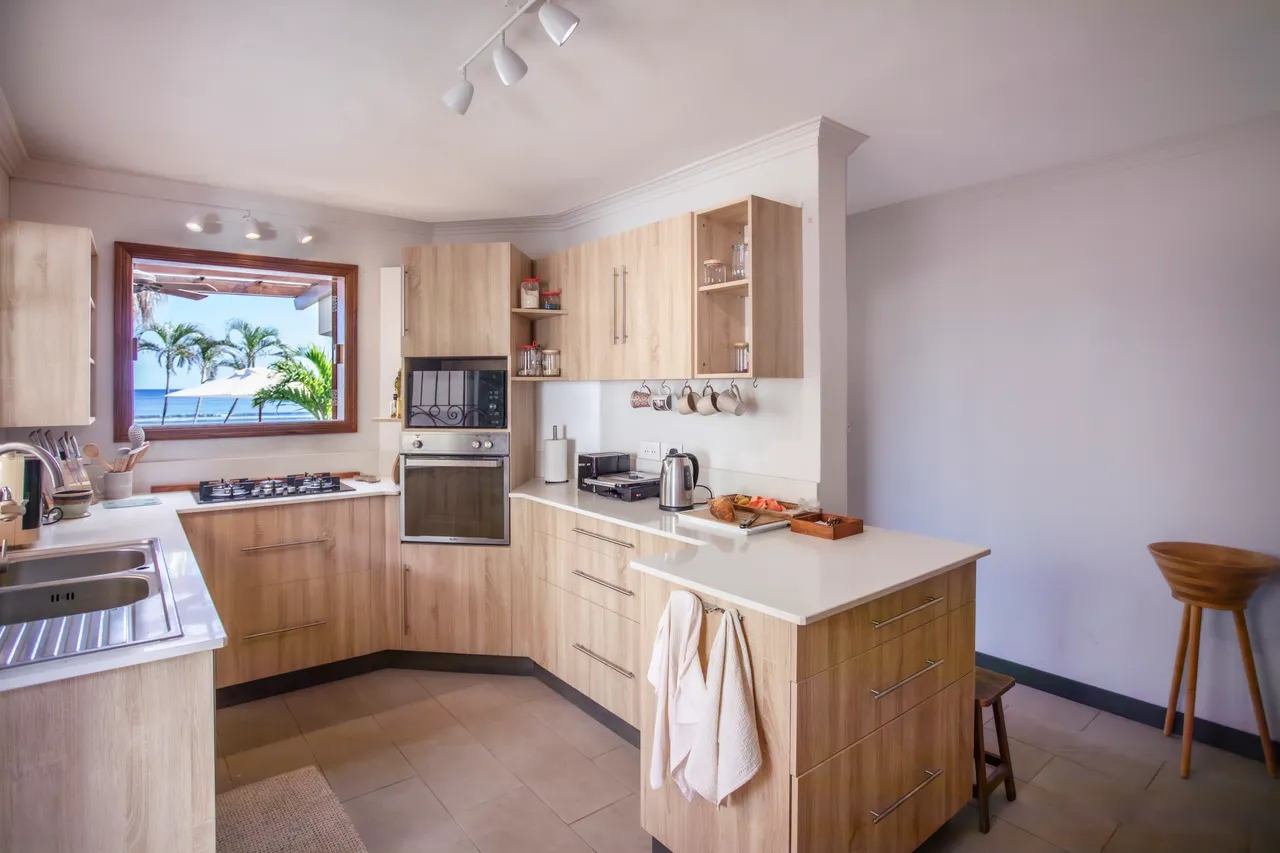 Cuisine équipée avec plans de travail en bois et appareils modernes. Fenêtre offrant une vue sur l'extérieur. Espace bar avec sièges fonctionnels.