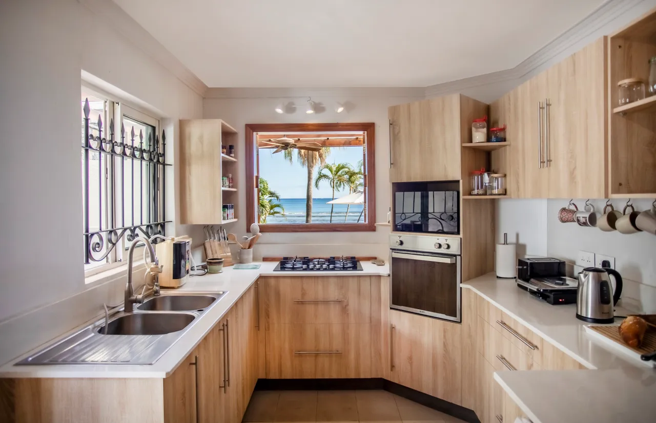 Cuisine lumineuse avec fenêtres offrant une vue sur la plage. Équipements modernes intégrés.