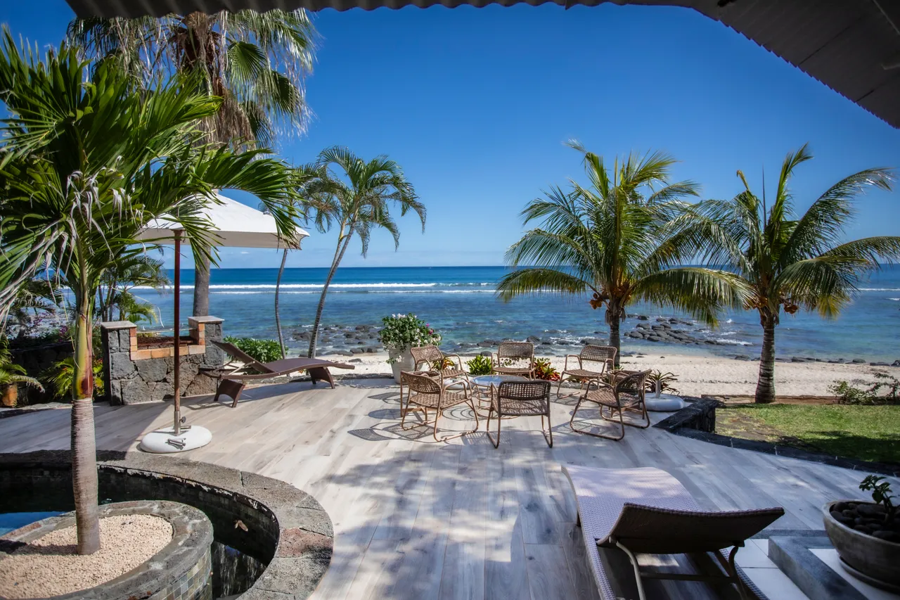 Terrasse spacieuse avec mobilier en rotin et vue sur la mer. Palmiers bordent l'espace extérieur.
