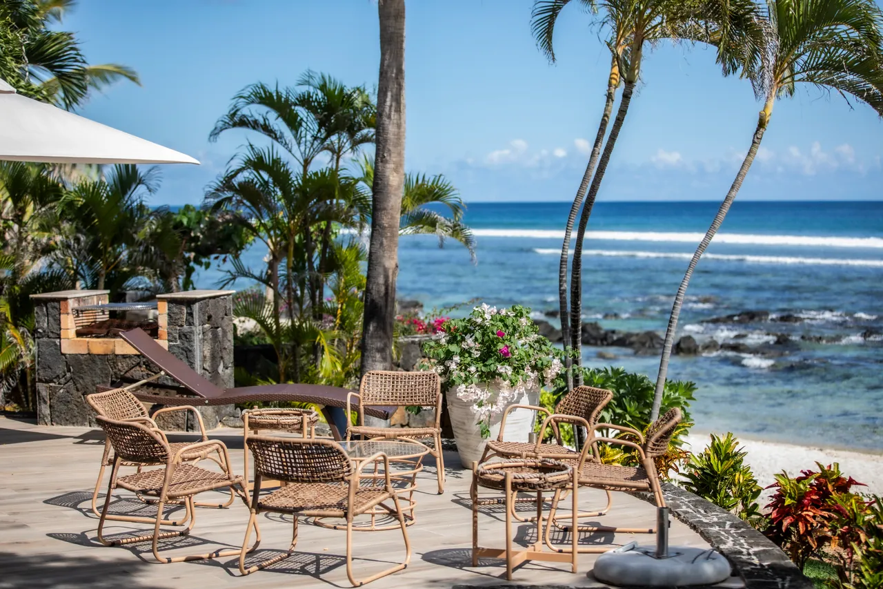 Terrasse en bois avec chaises en rotin, vue dégagée sur l'océan. Végétation tropicale en arrière-plan.