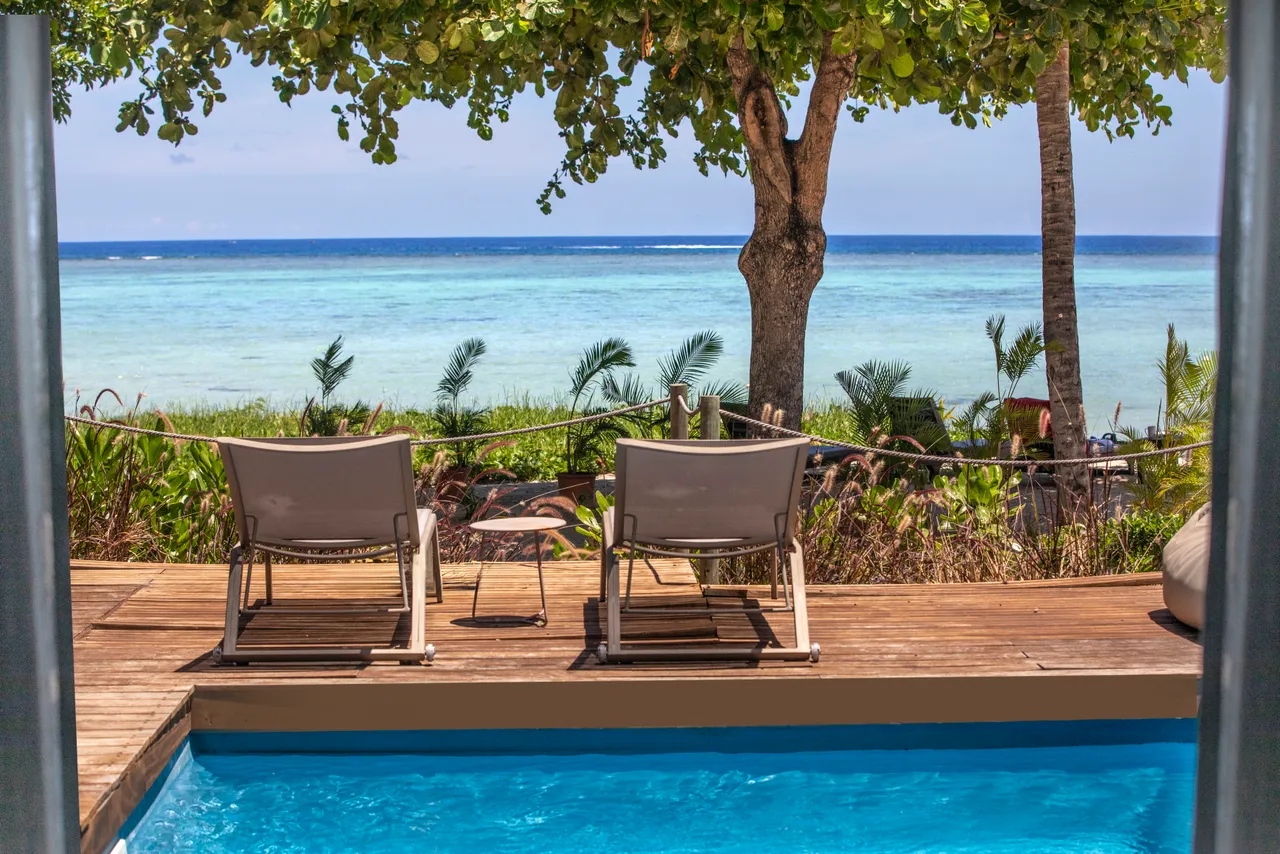 Tons de bleu et de vert en arrière-plan, avec des chaises longues au bord de la piscine.