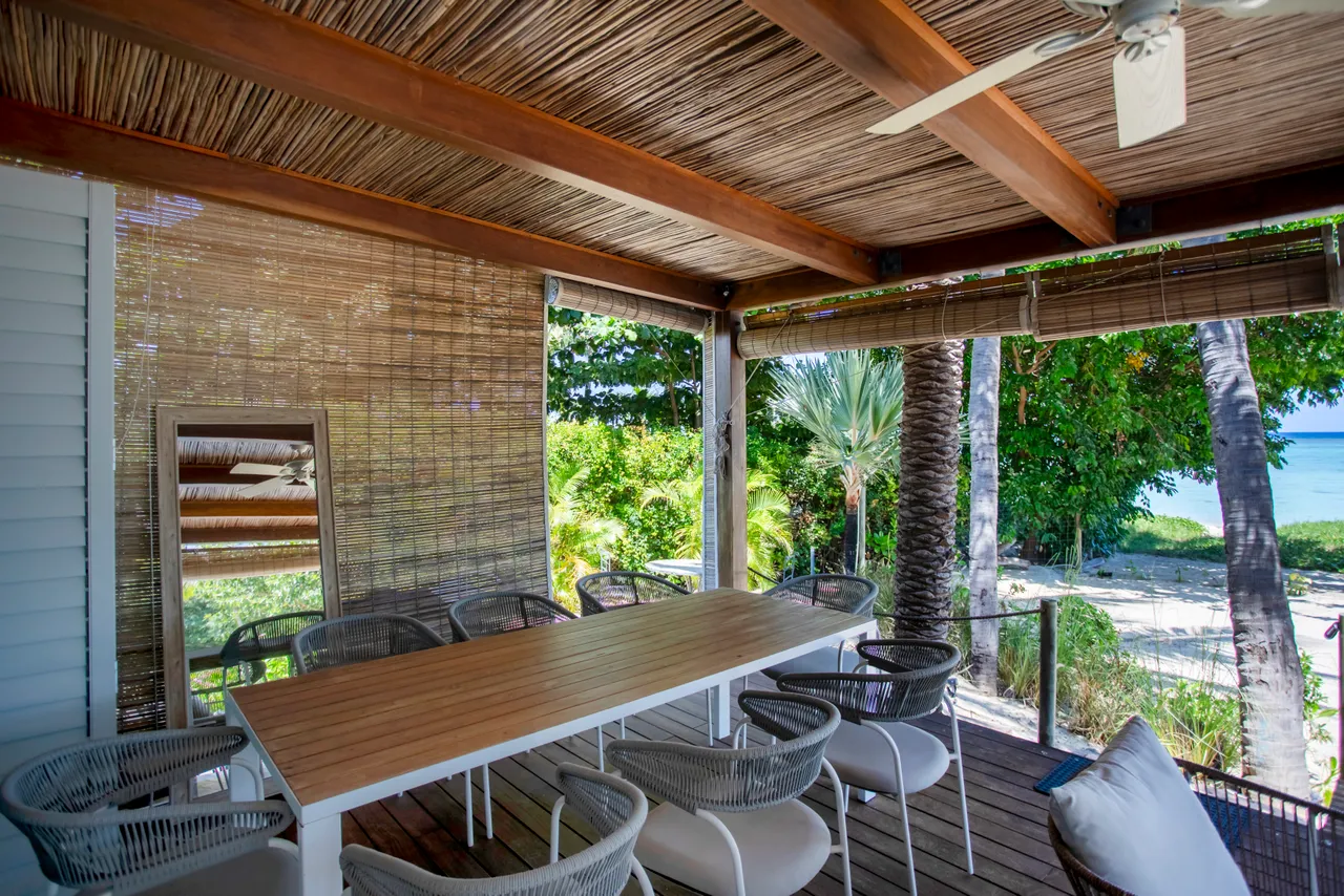 Espace repas extérieur avec table en bois et chaises en rotin. Ventilation naturelle grâce aux ouvertures.
