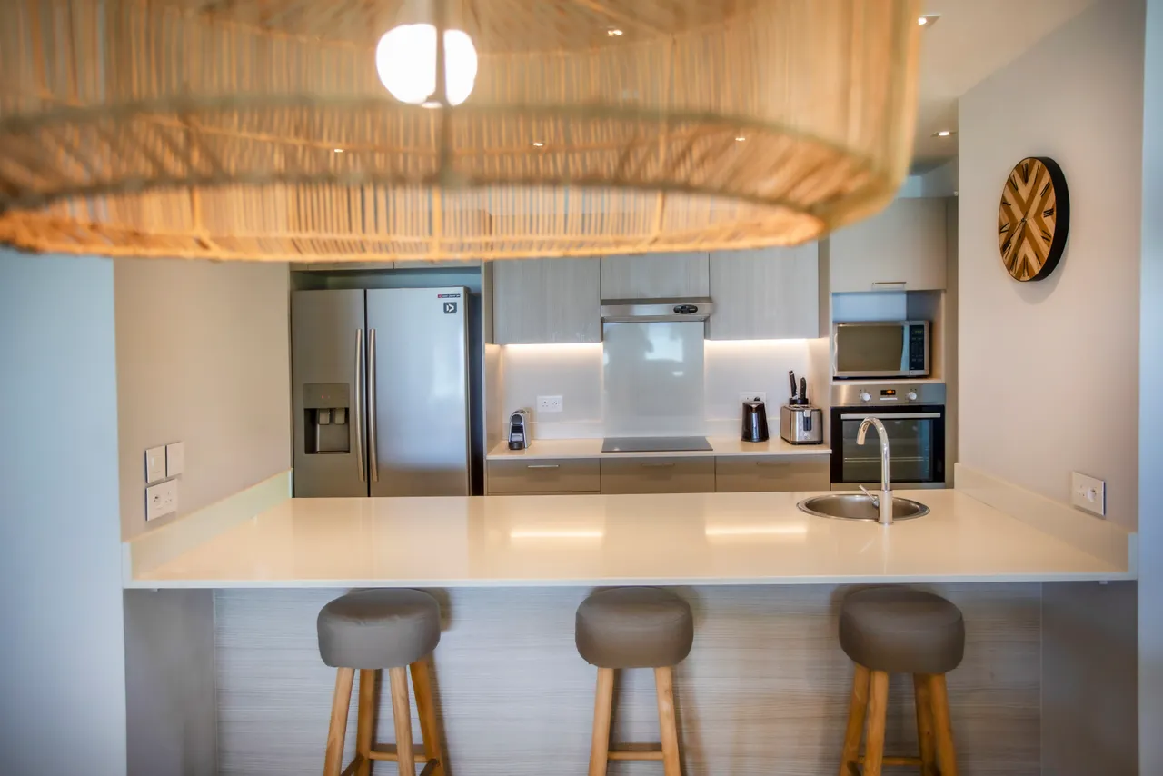 Cuisine moderne entièrement équipée avec un bar à petit-déjeuner. Éléments en bois ajoutent une touche chaleureuse. Électroménagers de qualité intégrés et luminaires en rotin. Espace fonctionnel et bien agencé.