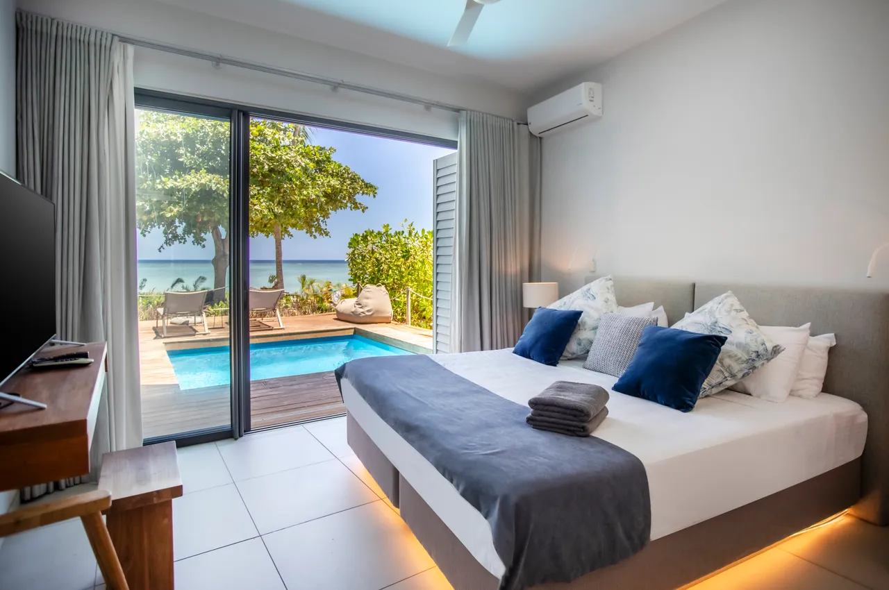 Chambre lumineuse avec vue sur la piscine privée et la mer. Lit double confortable et décor épuré. Accès direct à l'extérieur depuis la pièce.