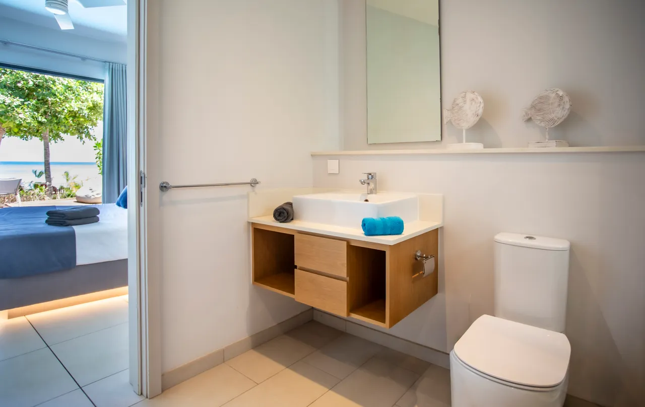 Salle de bain lumineuse avec lavabo sur meuble en bois. Éclairage doux et décor minimaliste. Accès direct depuis la chambre.