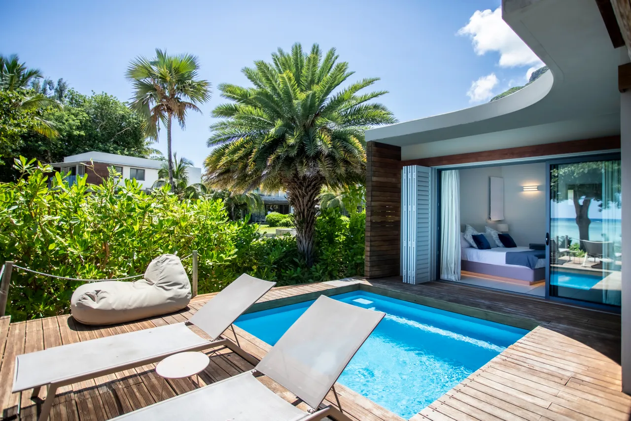 Espace extérieur avec chaises longues et petite piscine sur la terrasse. Vues dégagées sur la végétation environnante. Accès direct depuis la chambre à travers des portes vitrées.