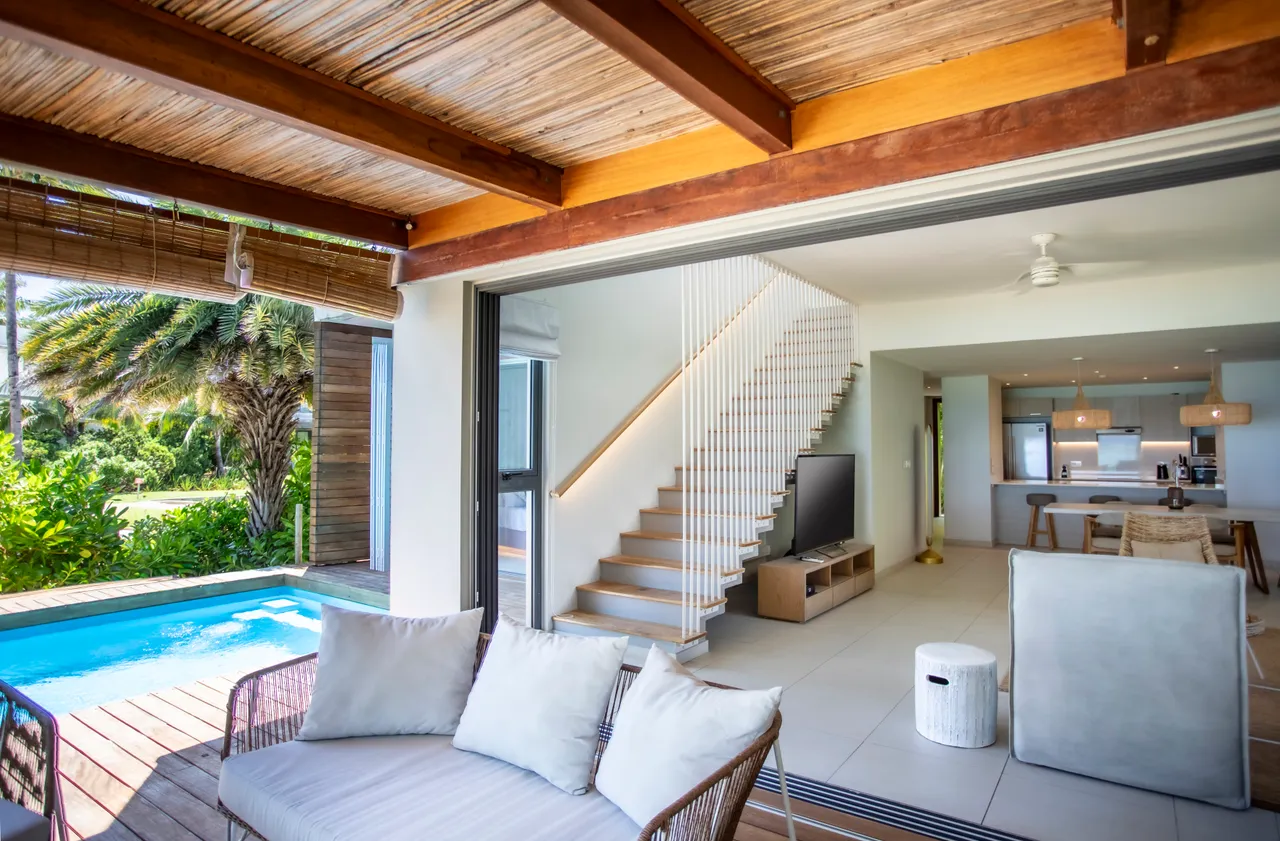 Ton bois naturel et teintes claires dans le salon créent une atmosphère apaisante. Espace ouvert avec accès direct à la piscine. Mobilier moderne et fonctionnel pour un confort quotidien. Grandes baies vitrées laissant entrer la lumière et offrant une vue sur l'extérieur.