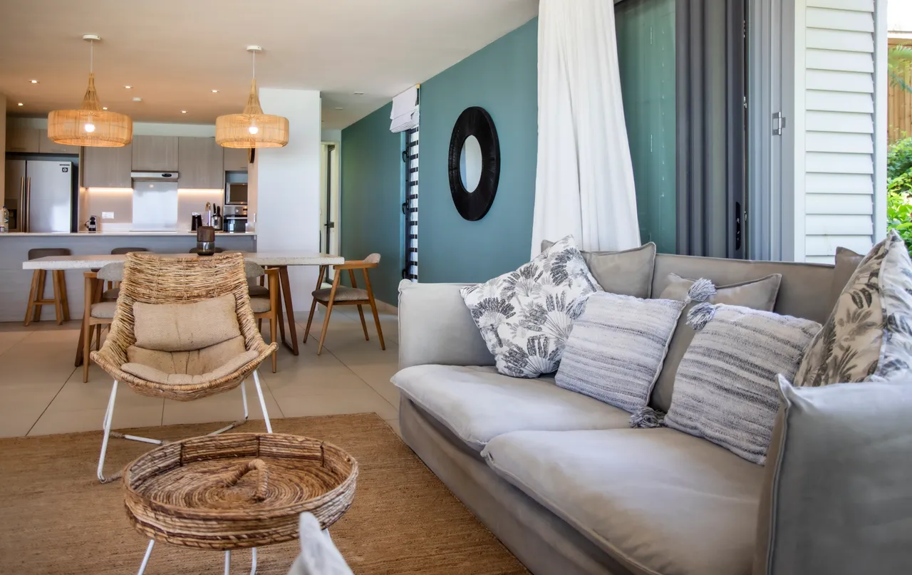 Lumière naturelle inondant le salon grâce aux grandes baies vitrées. Mobilier contemporain en harmonie avec des touches de bois. Espace ouvert menant à la cuisine et à la terrasse. Décoration minimaliste créant une atmosphère accueillante.