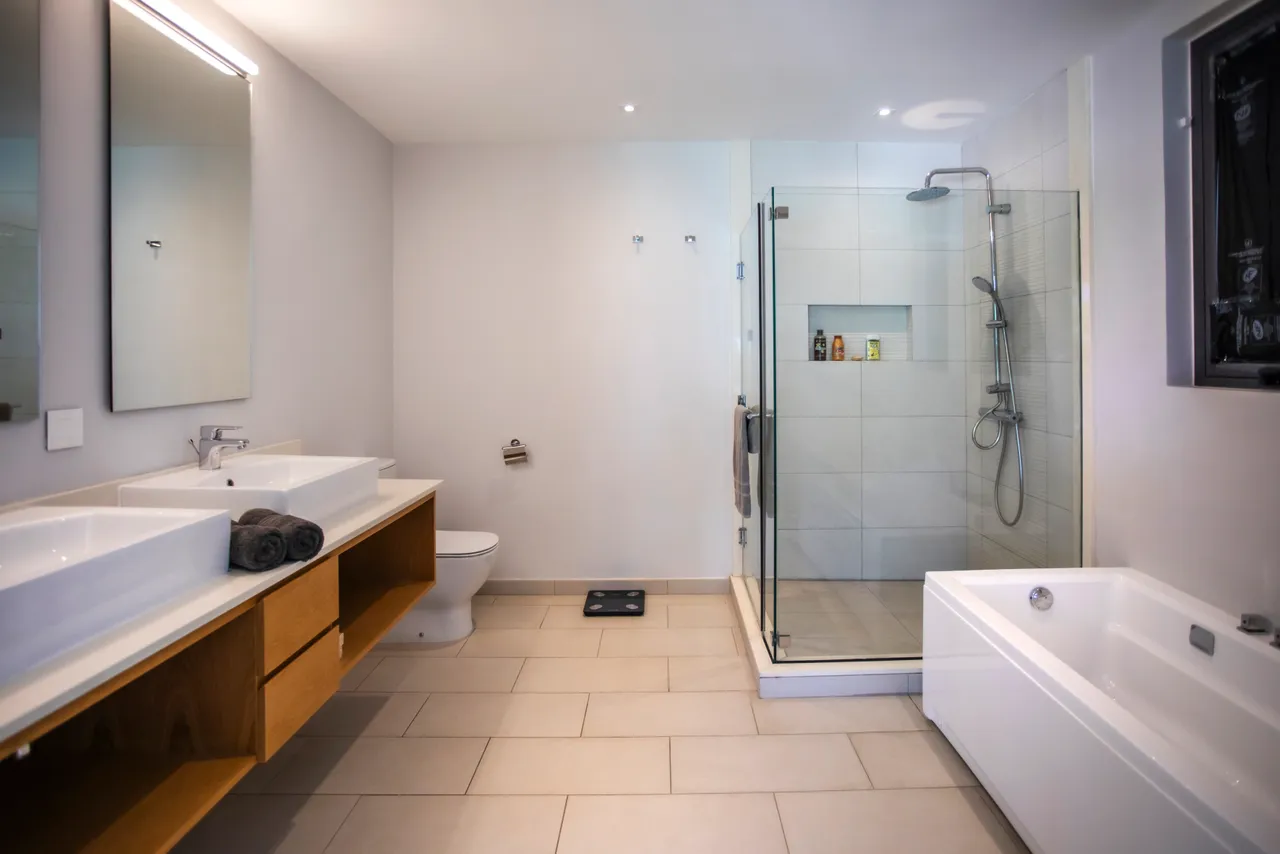 Salle de bain spacieuse avec douche à l'italienne et baignoire. Éclairage naturel provenant d'une fenêtre. Rangement intégré sous les lavabos en bois. Décoration épurée avec des lignes modernes.
