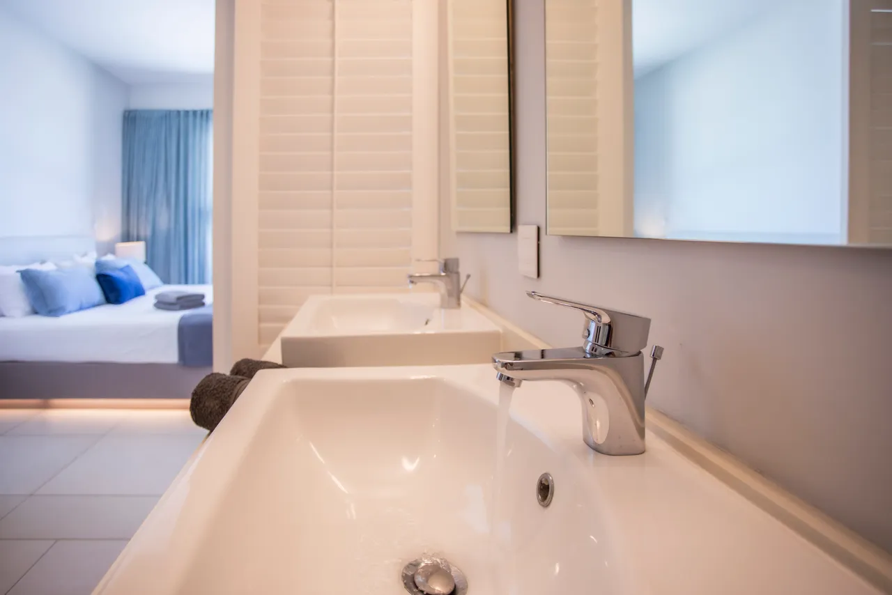 Teintes claires et surfaces épurées dans la salle de bain. Deux vasques pour plus de praticité. Éclairage naturel apporté par une fenêtre. Rangement intégré sous les lavabos en bois.