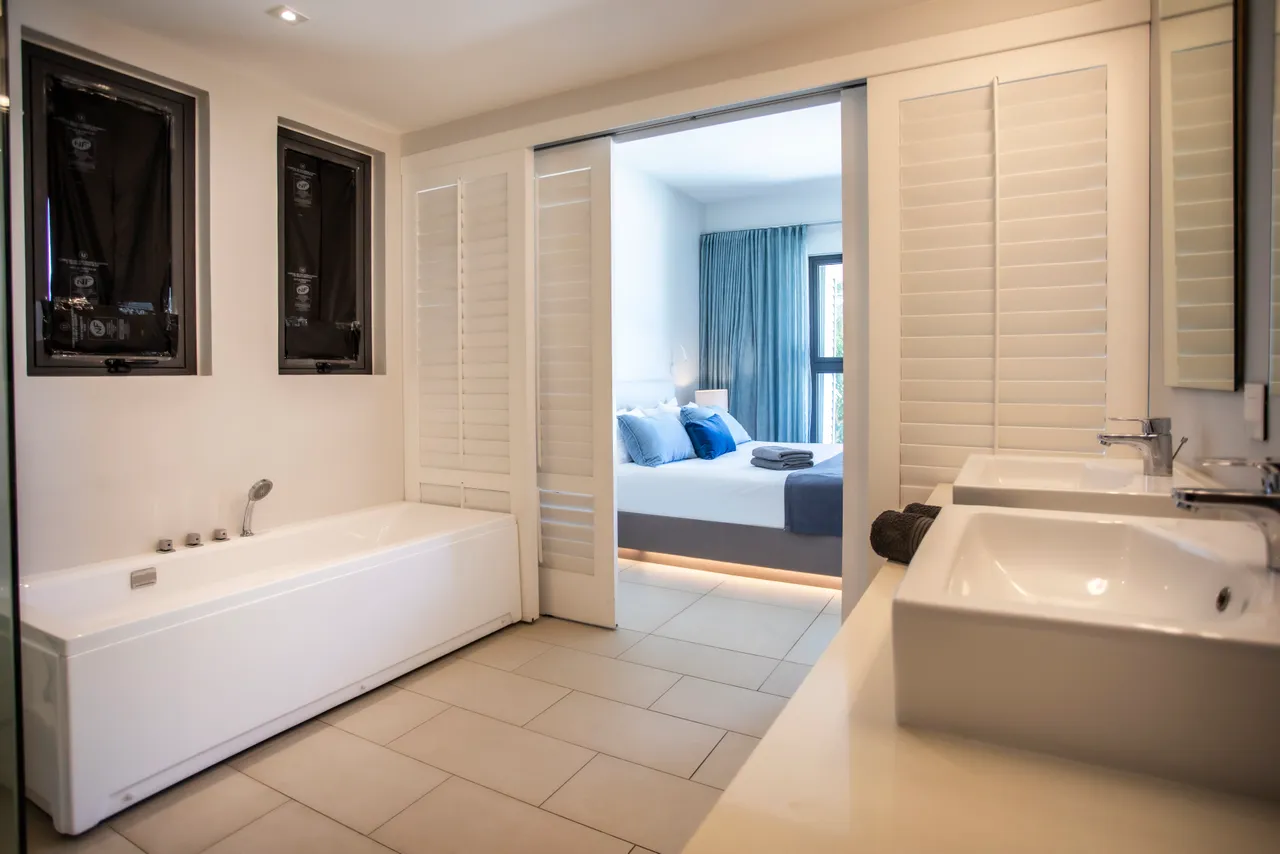Salle de bain avec baignoire et deux vasques sur un plan de travail. Éclairage naturel apporté par une fenêtre. Rangement intégré sous les lavabos en bois. Décoration épurée et moderne.