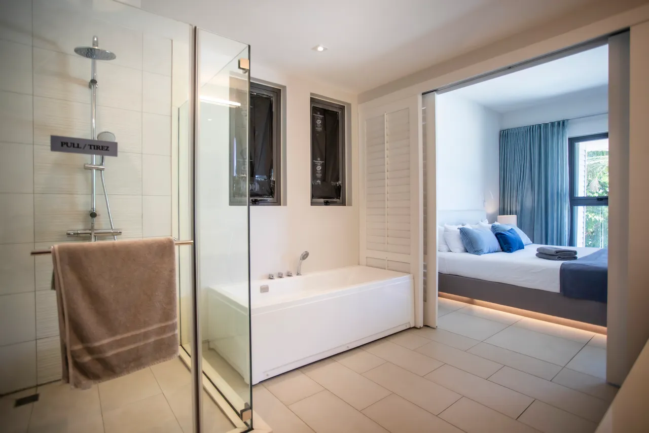 Salle de bain avec baignoire et douche à l'italienne. Éclairage naturel grâce à une fenêtre. Rangement sous les lavabos pour un espace pratique. Décoration moderne et épurée.