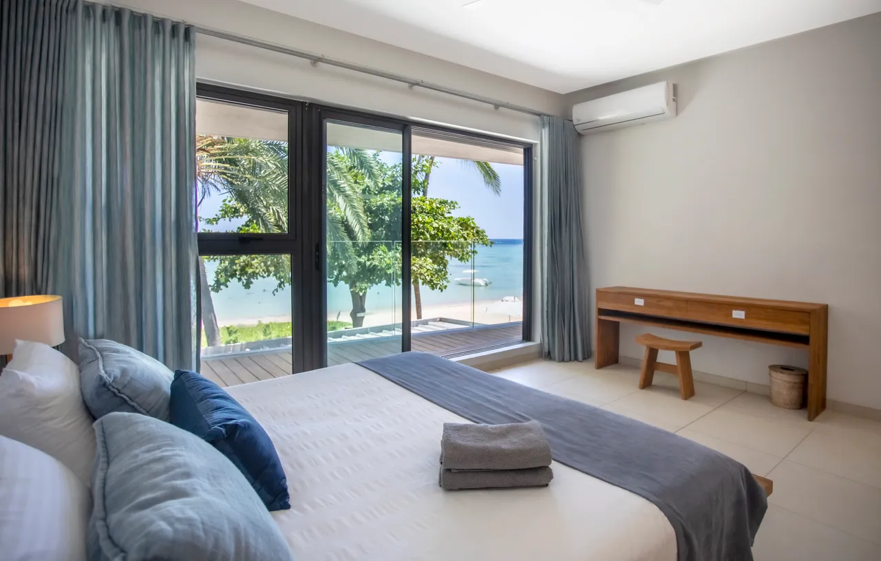 Chambre lumineuse avec lit double et vue sur la mer. Mobilier en bois clair et textiles neutres. Bureau fonctionnel et accès direct à l'extérieur. Grandes fenêtres assurant un éclairage naturel.