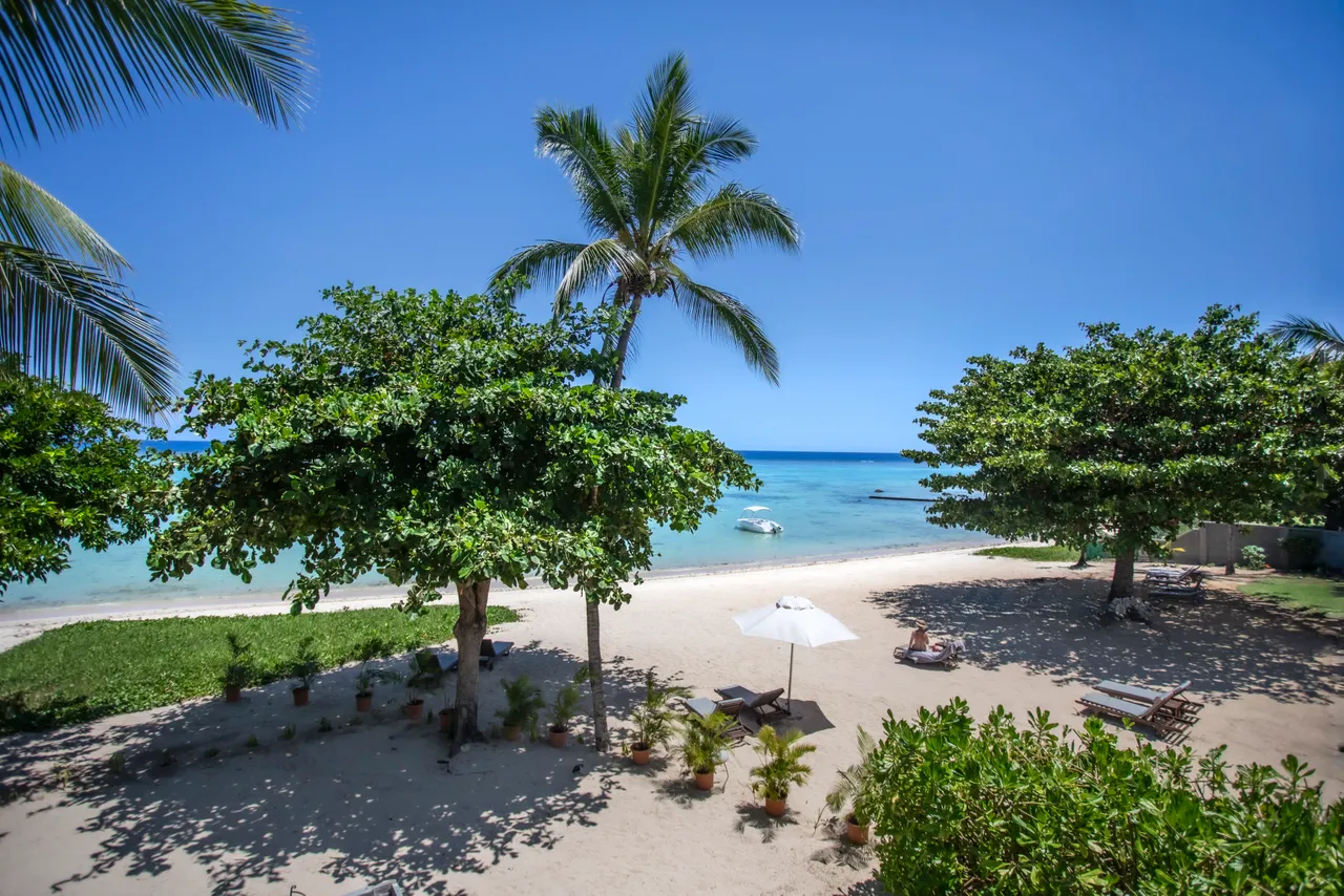 Plage privée avec parasol et chaises longues pour se détendre. Végétation tropicale offrant de l'ombre naturelle. Accès direct à l'eau depuis le sable. Espace extérieur spacieux et accueillant.