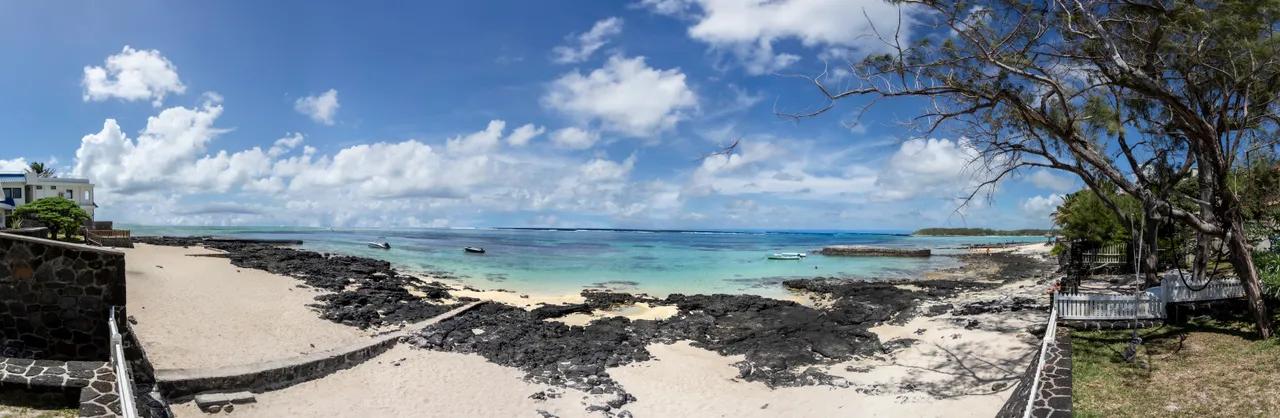 Teintes sableuses et marines, accès direct à la plage depuis le jardin. Espace extérieur avec rochers et vue panoramique sur l'océan.