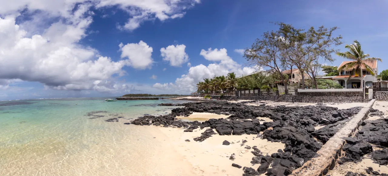 Vue panoramique de la plage avec rochers et eau turquoise. Palmiers bordent le rivage.