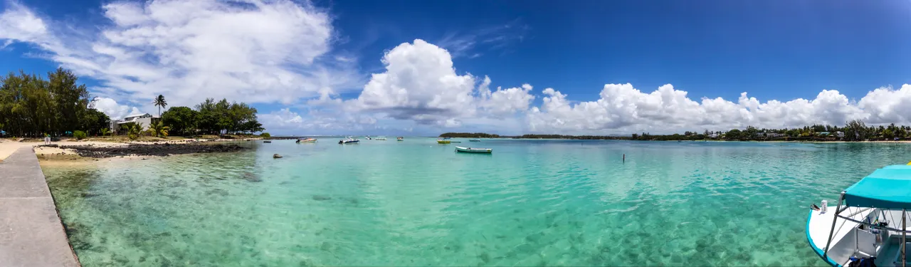 Vue sur la mer avec bateaux amarrés et eaux turquoise. Ciel partiellement nuageux au-dessus.