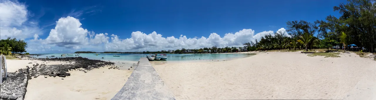 Plage de sable fin avec eaux turquoise et rochers. Ciel dégagé et nuages épars.