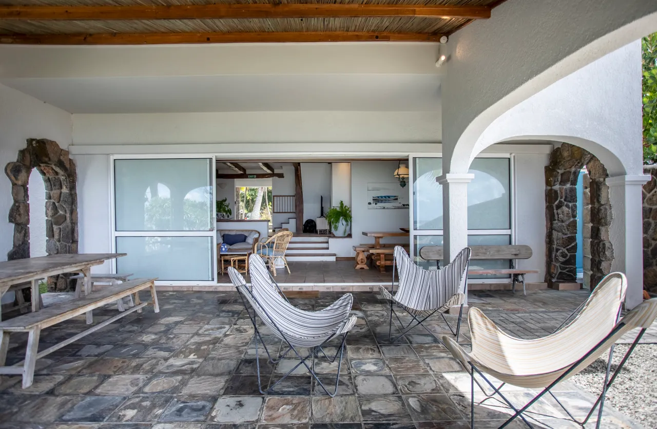 Sol en pierres naturelles, espace couvert avec chaises en tissu. Ouverture sur un intérieur lumineux et aéré.