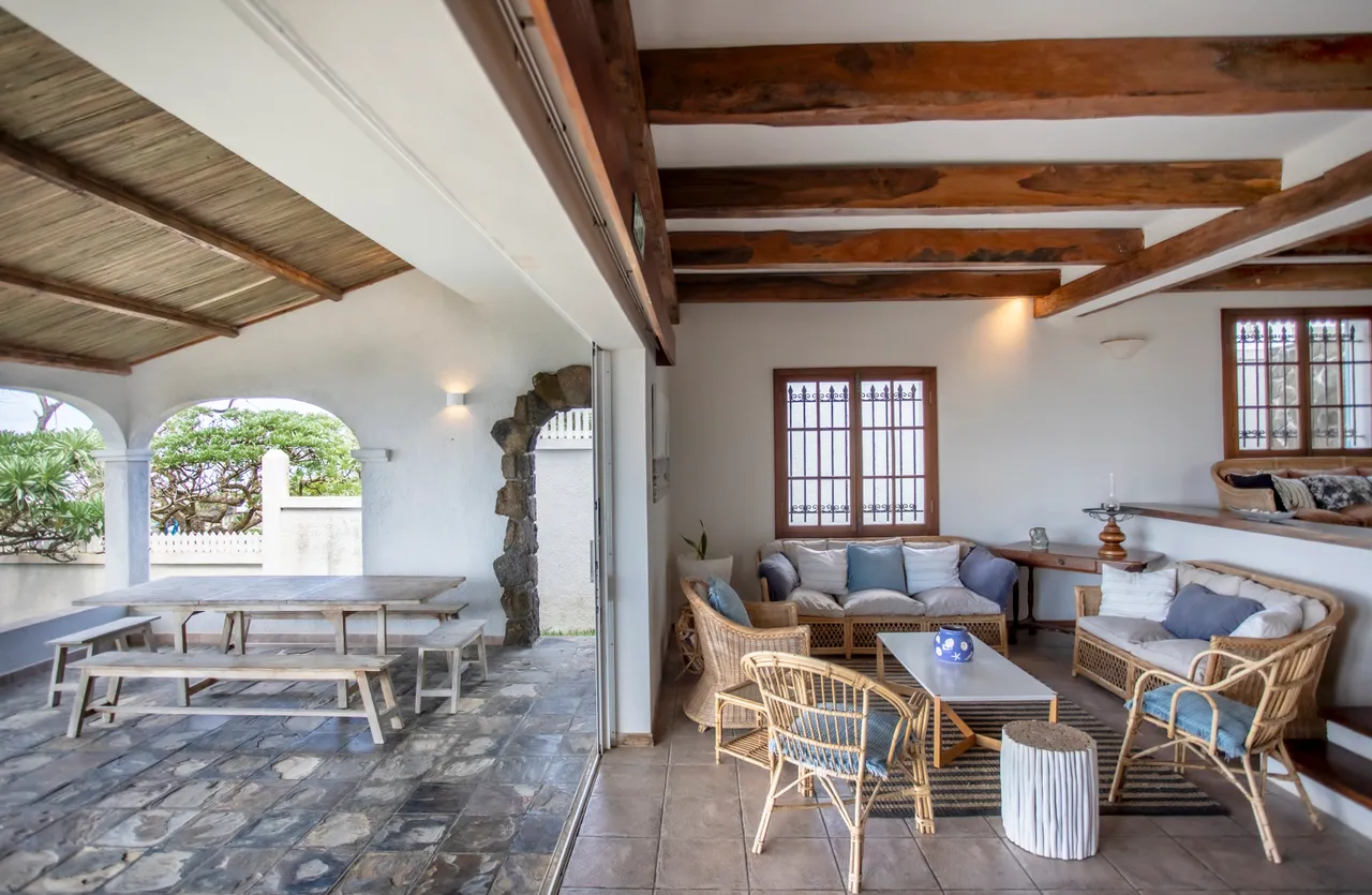 Espace intérieur lumineux avec poutres en bois et mobilier en rotin. Vue sur le jardin depuis le salon.