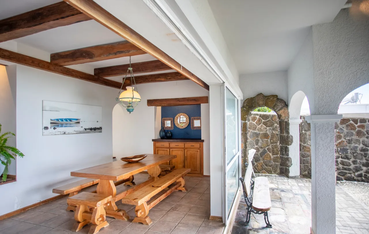 Galerie. Grande table en bois avec bancs, décor en pierre et poutres apparentes. Espace lumineux avec fenêtres.