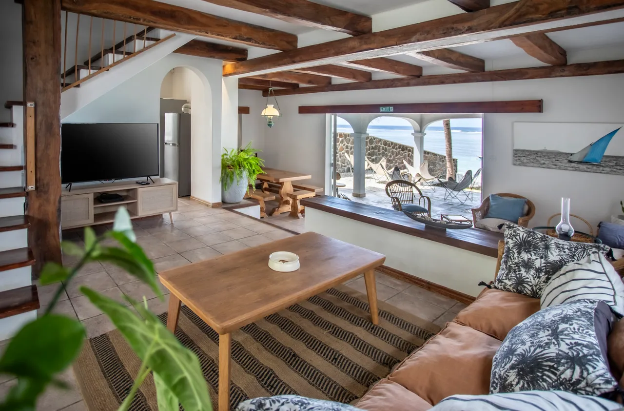Teintes neutres et bois, espace de vie avec canapés et télévision. Grande baie vitrée donnant sur la mer.