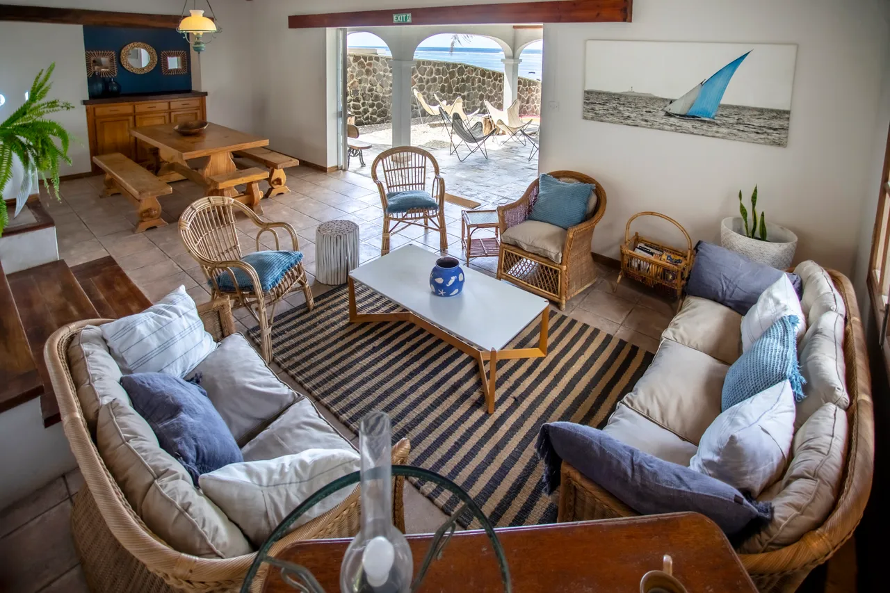 Espace de vie avec sièges en rotin et tapis rayé. Accès direct à la terrasse.