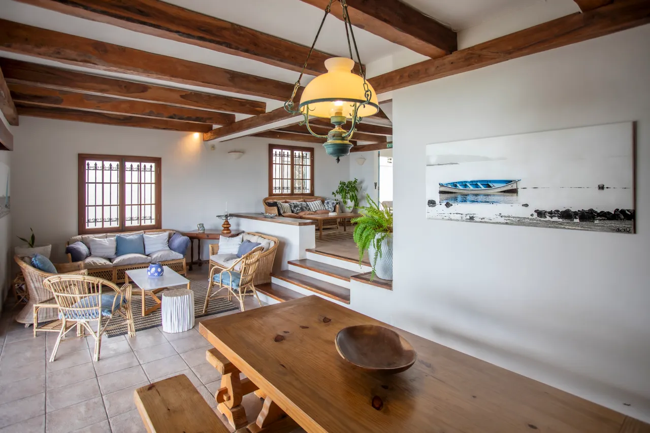Espace ouvert avec poutres en bois et coin salon. Mobilier en rotin et vue sur l'extérieur.