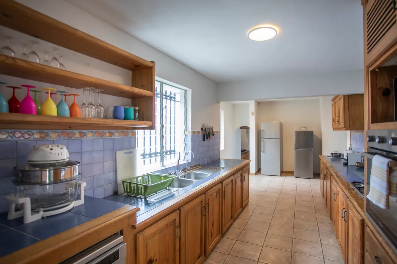 Cuisine spacieuse avec plans de travail en carrelage et rangements en bois. Équipements électroménagers accessibles.