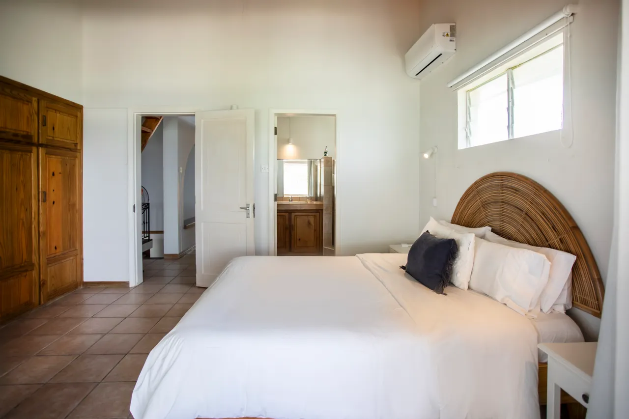 Chambre. Lit double avec tête de lit en rotin et rangement intégré. Luminosité naturelle grâce aux fenêtres.