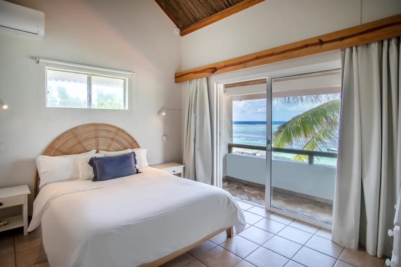 Chambre avec lit double et accès à un balcon vue mer. Décor en bois et lumière naturelle.
