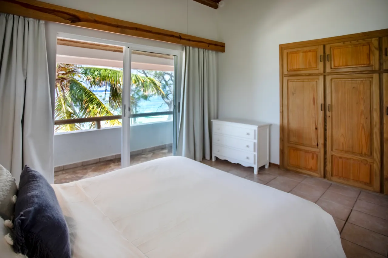 Chambre. Lit double avec rangement et grande fenêtre donnant sur le balcon. Decor minimaliste avec murs clairs.