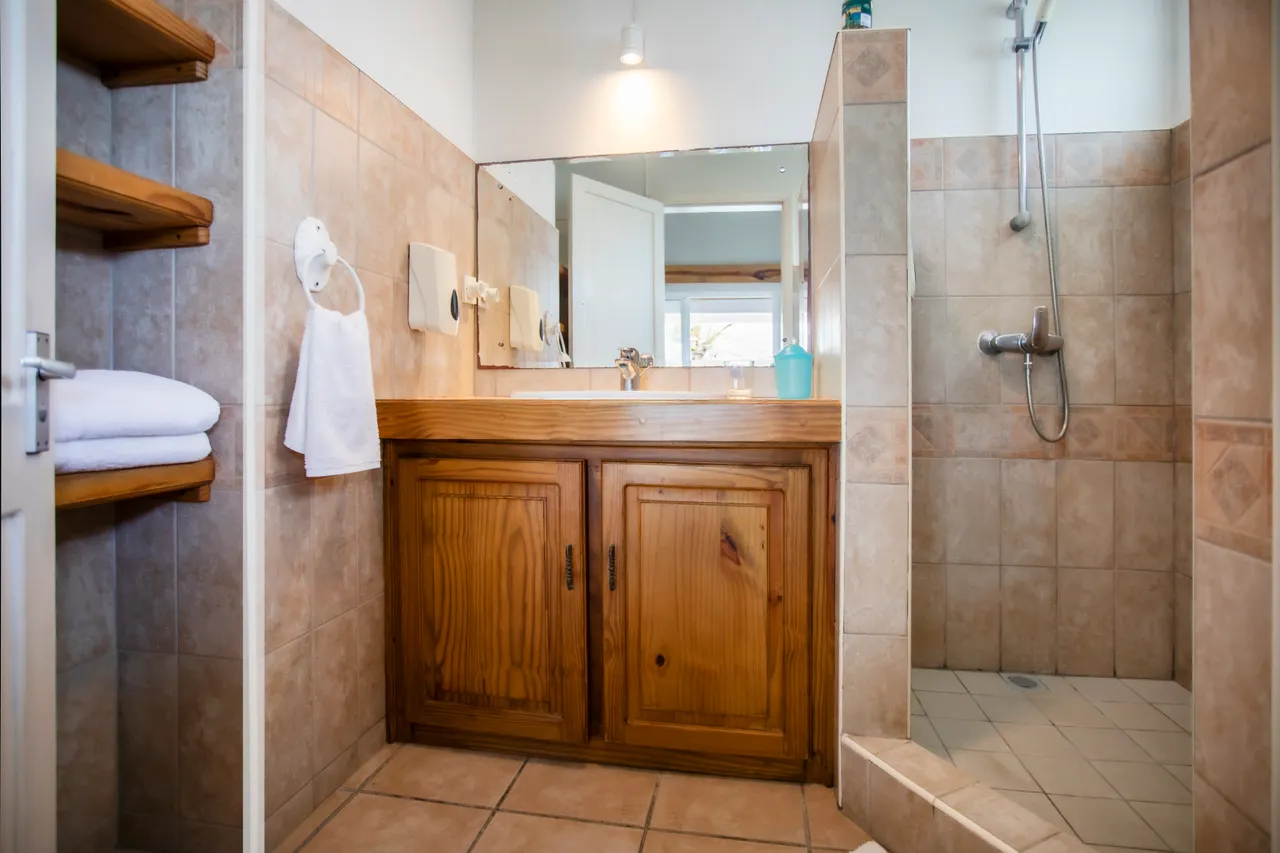 Salle de bains. Douche spacieuse avec carrelage et lavabo en bois intégré. Étagères pour rangement.