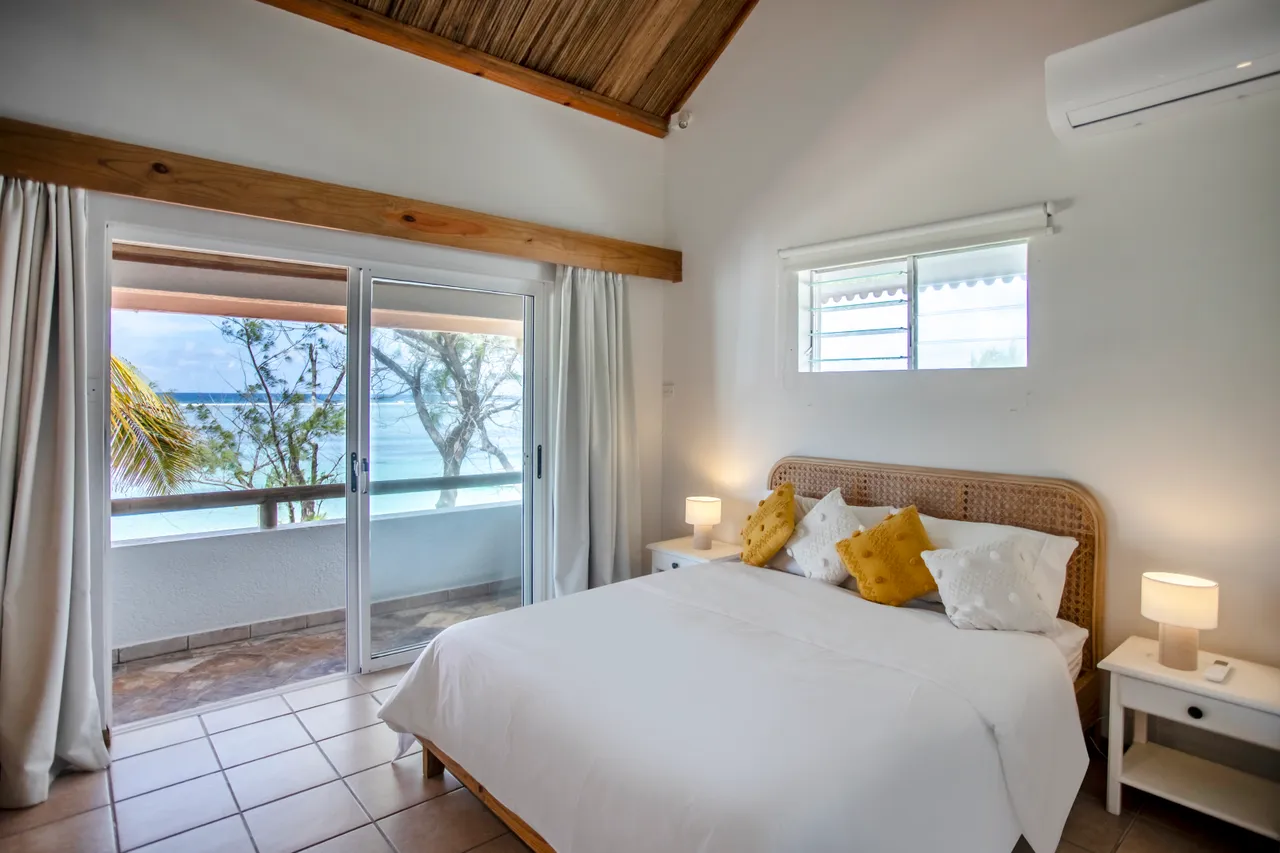 Chambre avec lit double et éclairage naturel depuis les fenêtres. Accès à un balcon avec vue sur la mer.