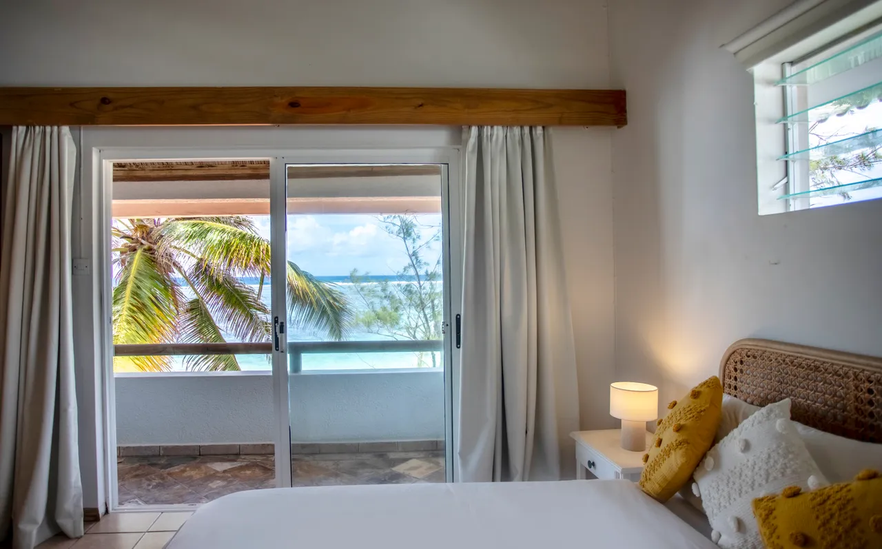 Galerie. Accès à un balcon avec vue sur la mer et grandes fenêtres. Décoration simple avec éclairage naturel et mobilier en rotin.
