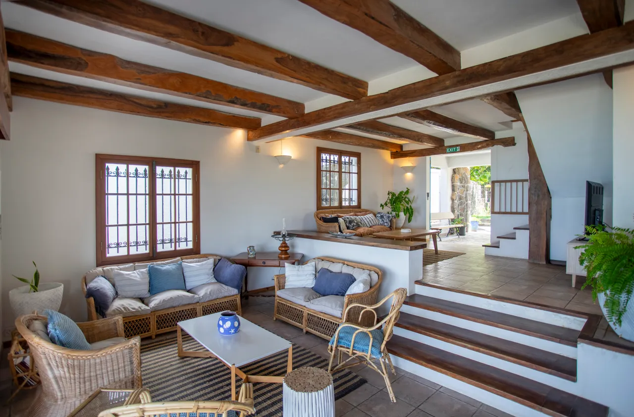 Bois naturel et lumière douce, espace de vie avec canapés en rotin. Plafond à poutres apparentes et accès direct à la terrasse.