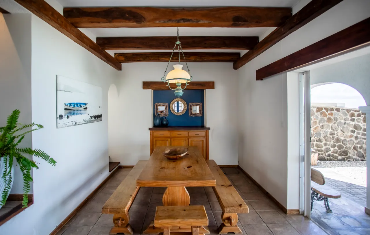Salle à manger. Table en bois massif avec bancs, décor simple et poutres apparentes.