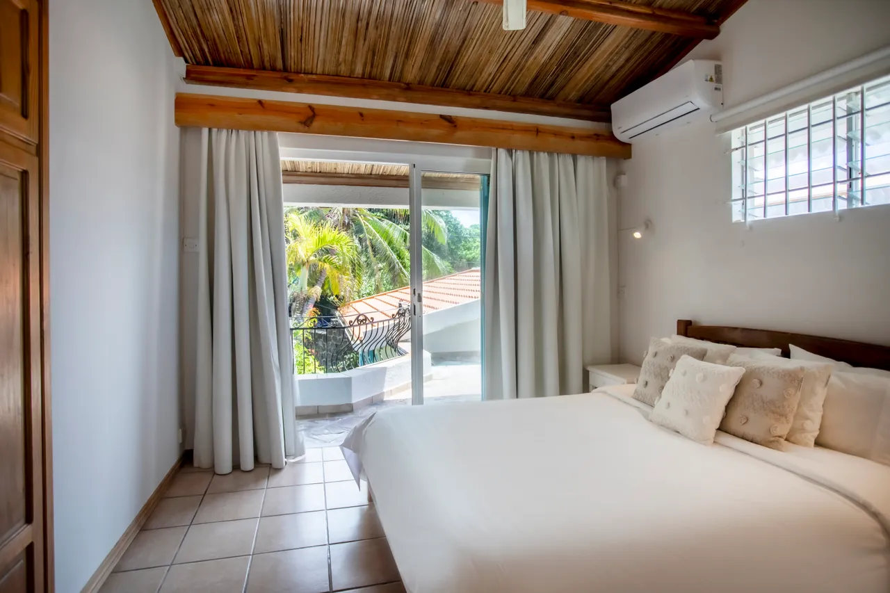 Chambre avec lit double et accès direct à un balcon. Espace lumineux avec portes-fenêtres et plafond en bois.