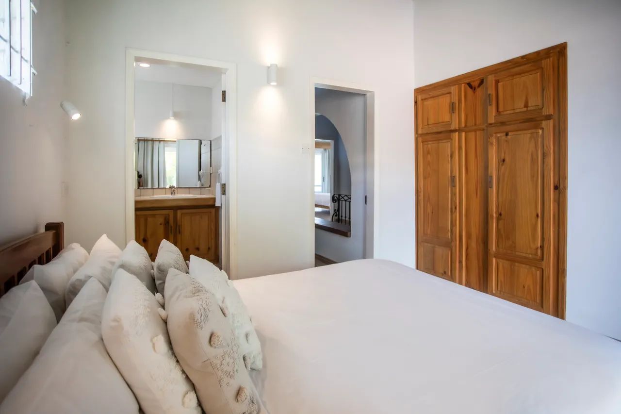 Chambre avec lit double et placard en bois. Éclairage naturel provenant des fenêtres.